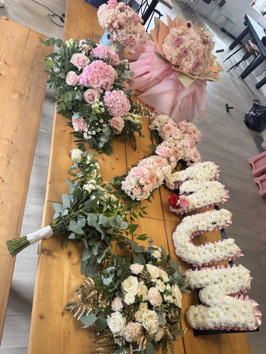 A letter tribute in white flowers beside a white rose spray and a pink hydrangea spray