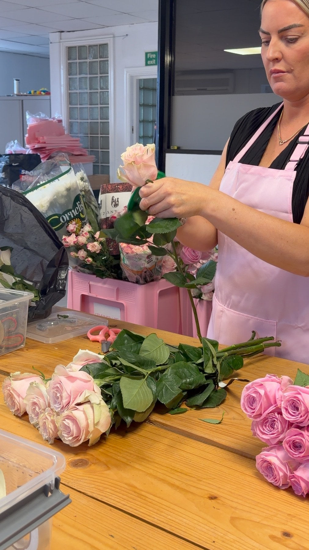 A student holding a single pink rose while building a bouquet