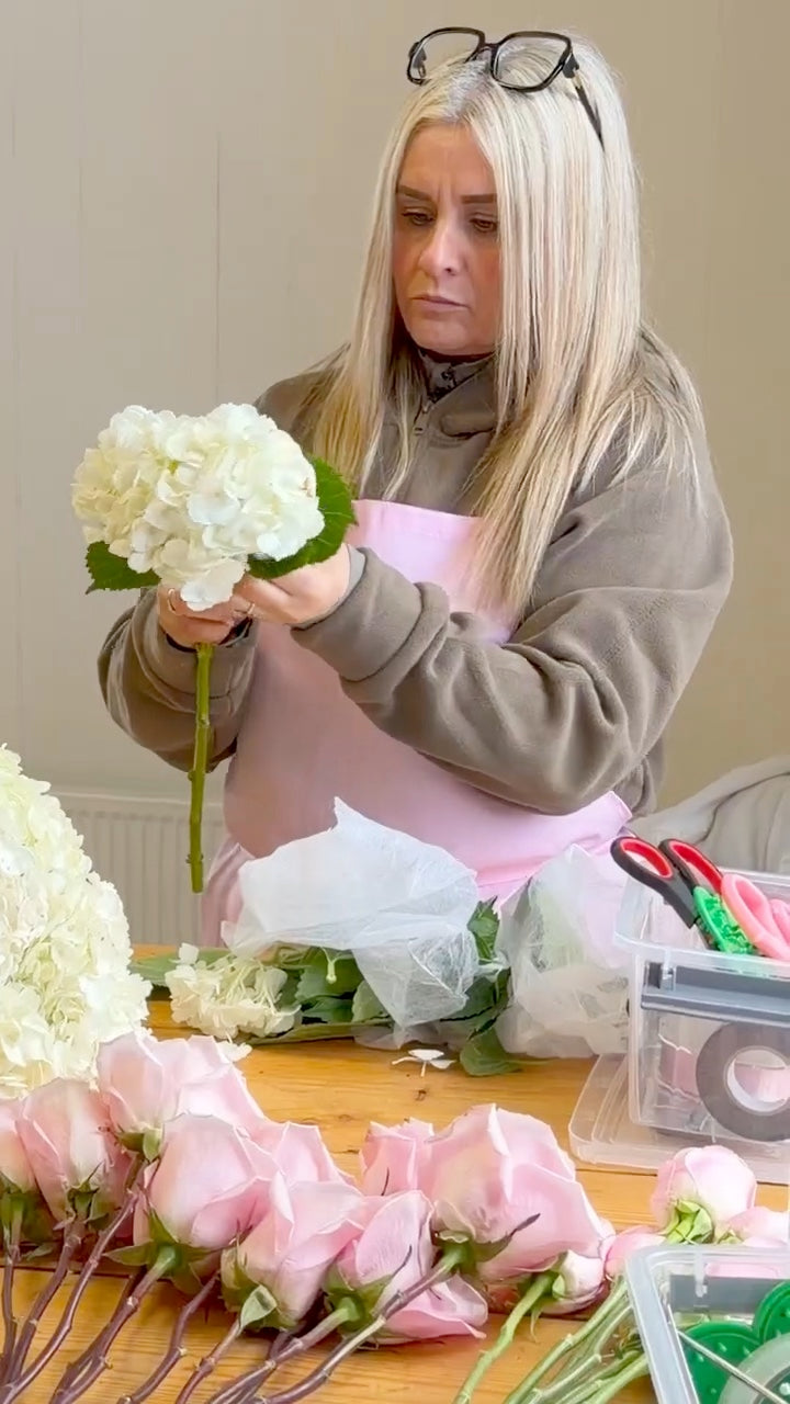 A student making a hydrangea and rose bouquet at the workshop table
