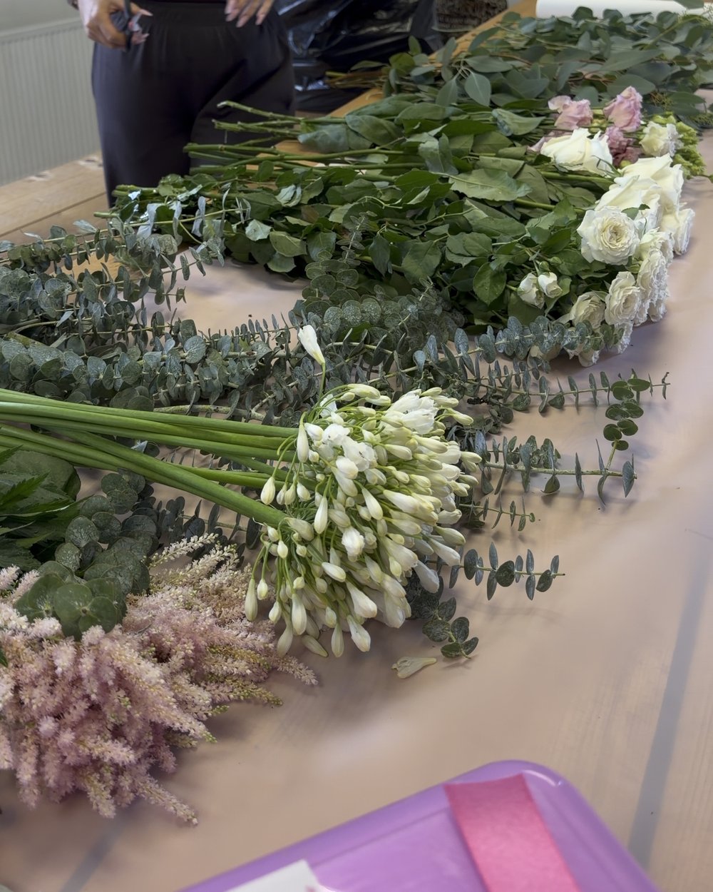 White roses, eucalyptus and pink stems laid out ready to build with