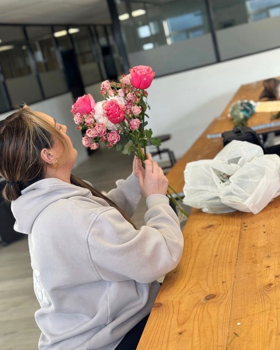 A bride-to-be holding a bunch of pink roses at the workshop table