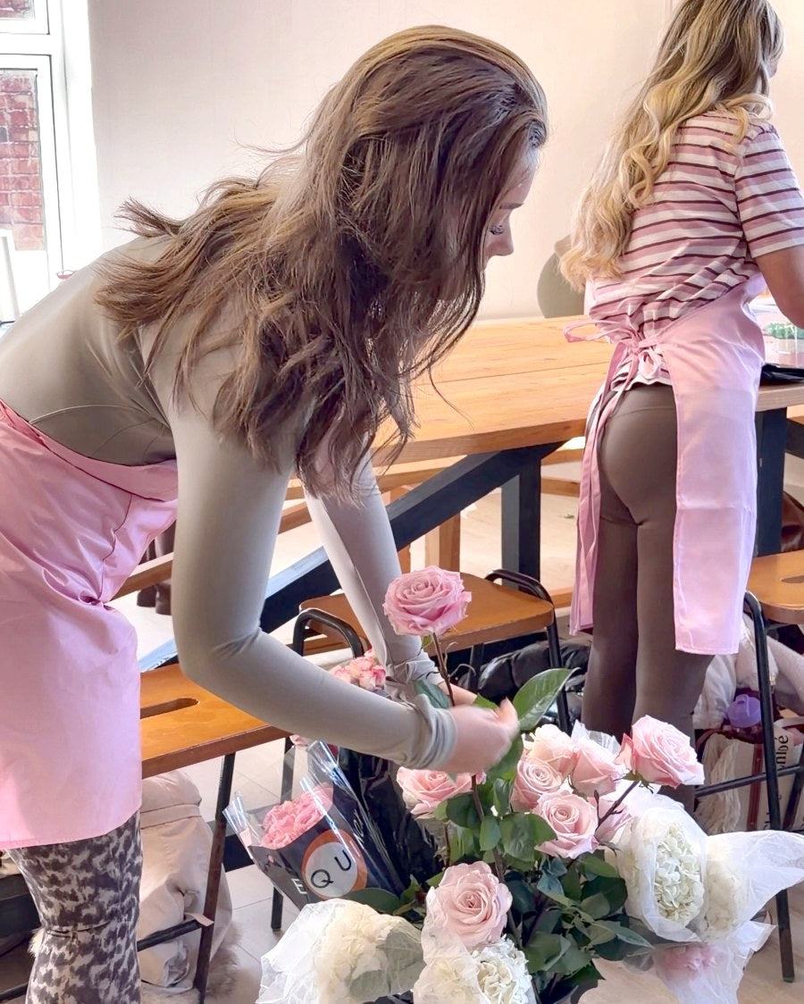 Two students leaning over the table to build a pink bouquet