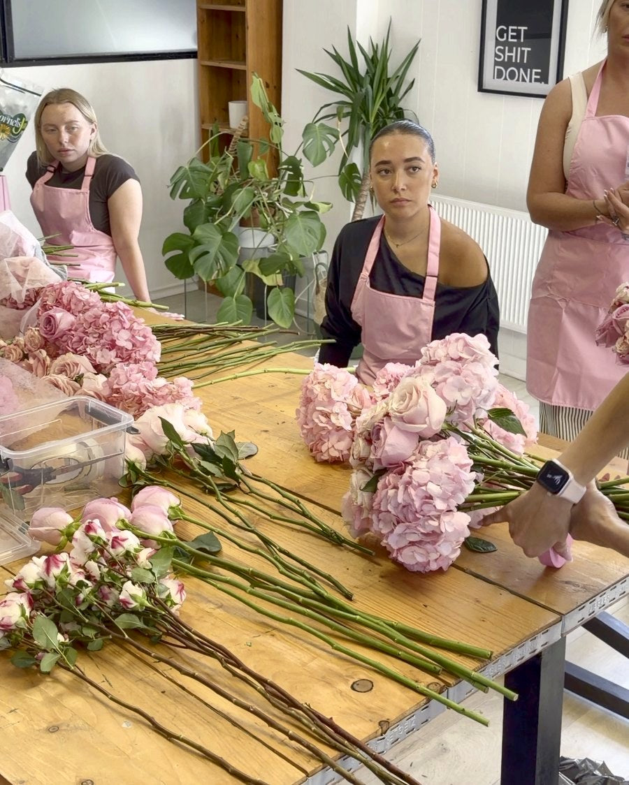 Students arranging pink hydrangeas and roses along the table