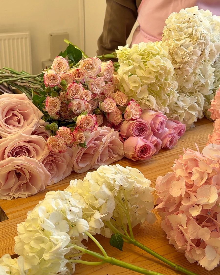 Pink roses and hydrangeas laid out on the table, ready to be made into bouquets