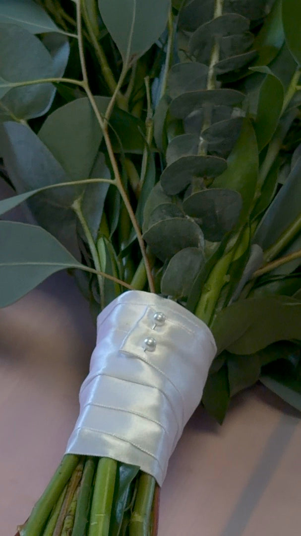 A satin ribbon wrap with pearl pins on a bouquet handle