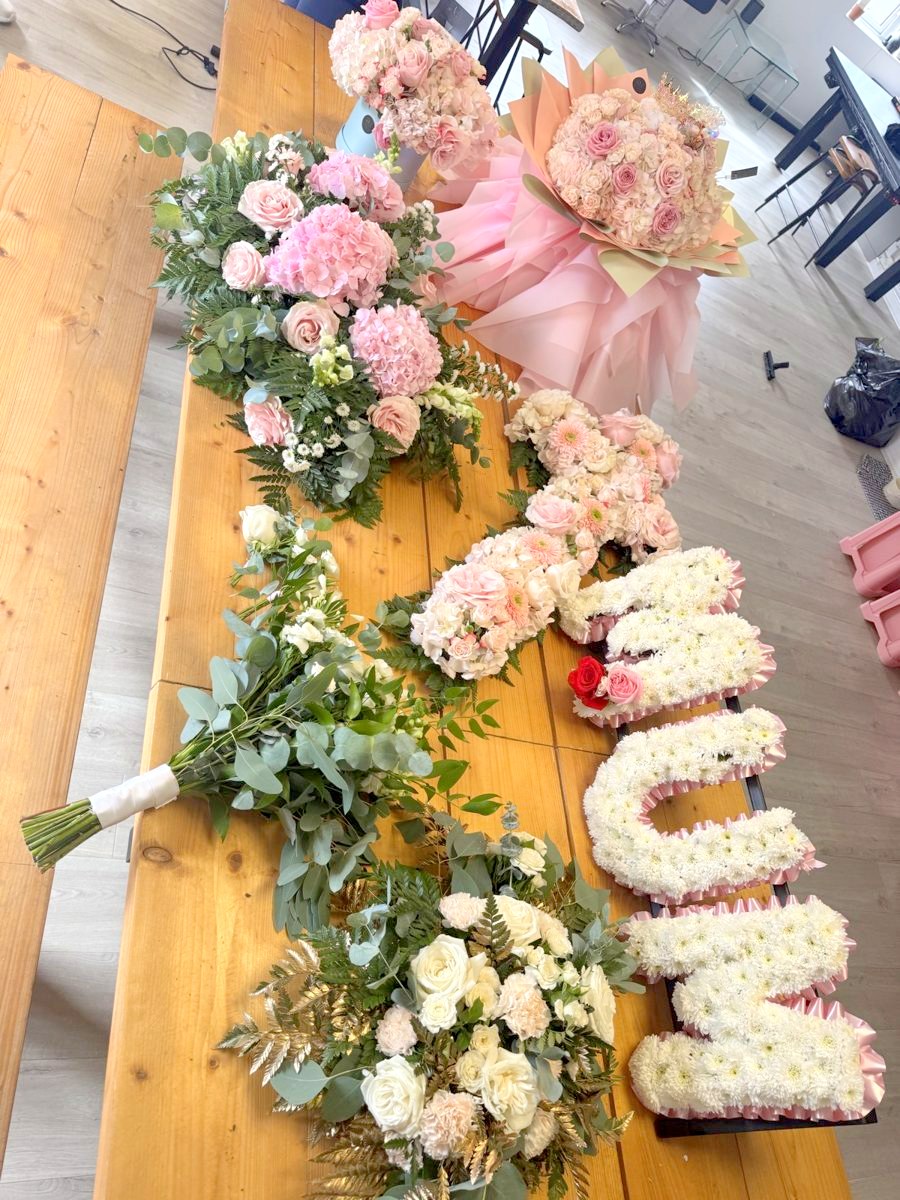 A letter tribute in white flowers beside a white rose spray and a pink hydrangea spray