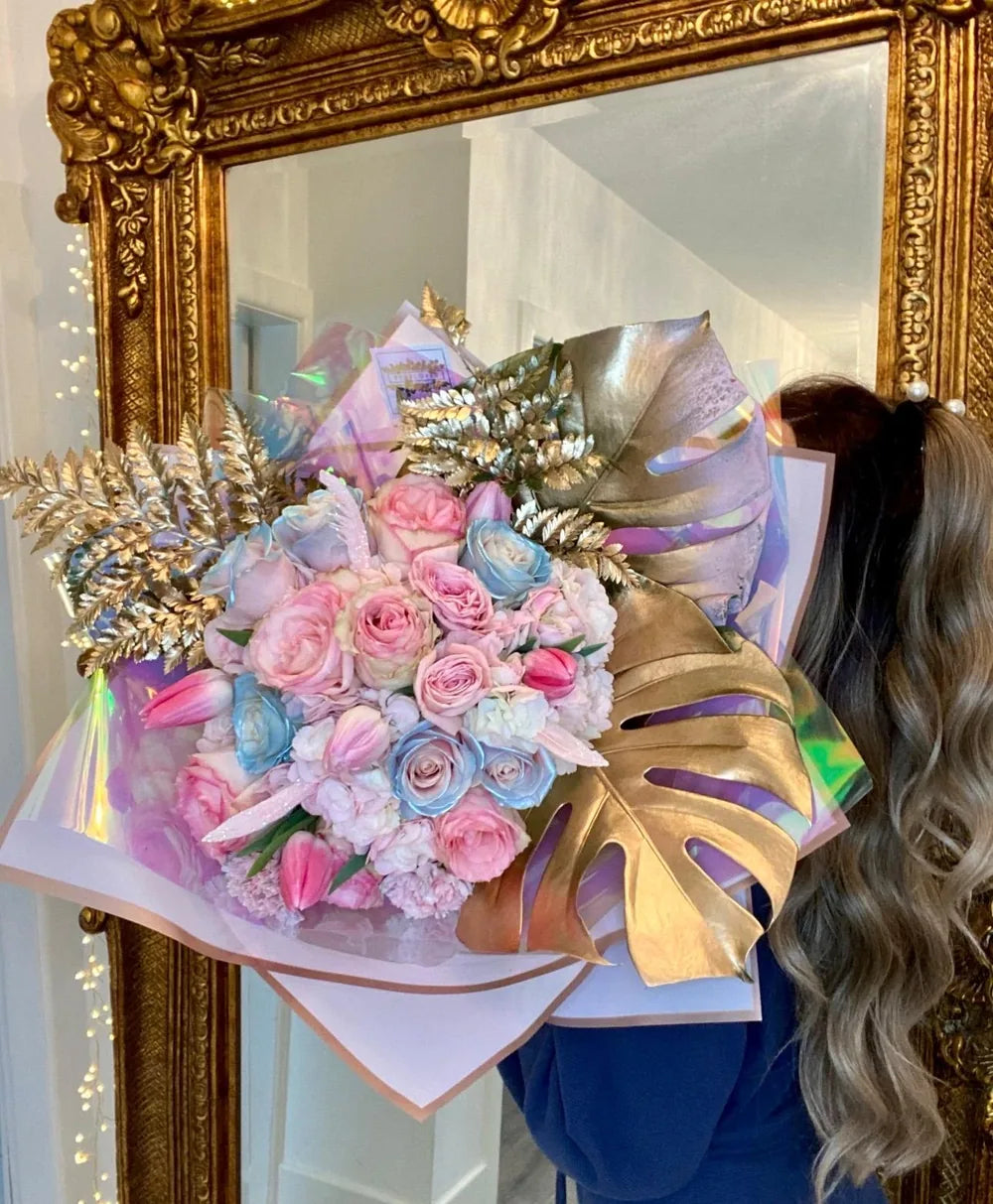 The fairytale bouquet, pink and blue roses with gold leaves, held up in front of a gold mirror