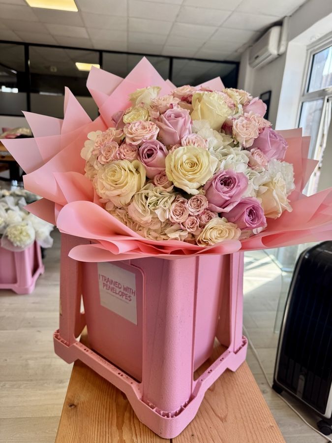 A finished pink and cream rose bouquet in a branded pink box
